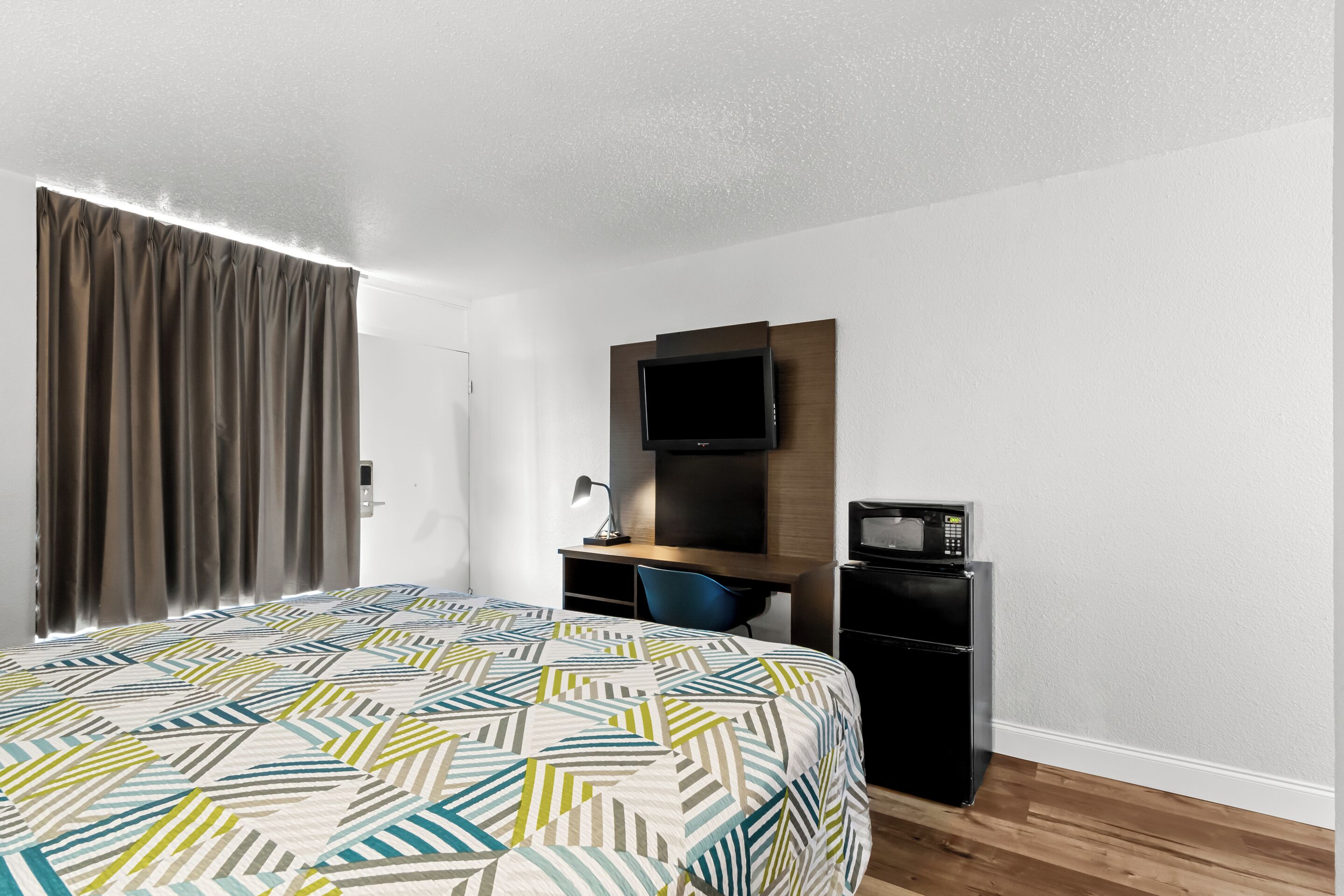 A hotel room with a bed, a desk, a television, and a refrigerator.