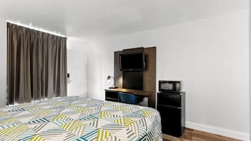 A hotel room with a bed, a desk, a television, and a refrigerator.