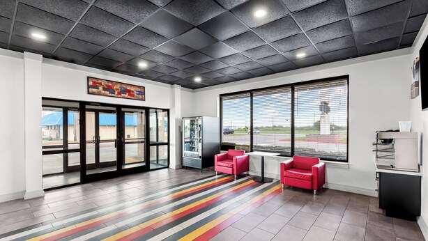 A modern lobby with a checkered ceiling, large windows, a vending machine, and red seating. - Motel 6 Port Lavaca, TX (Port Lavaca)