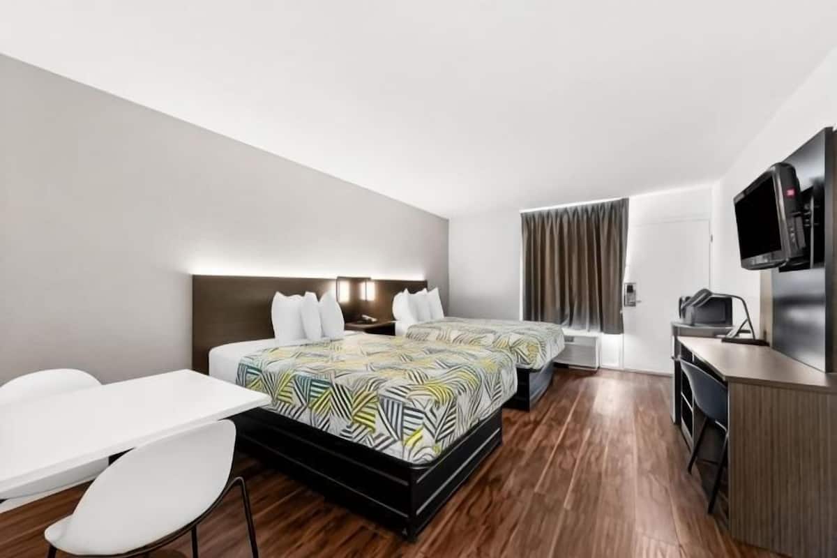 A hotel room with a bed, a desk, a chair, a TV, and a window with curtains.
