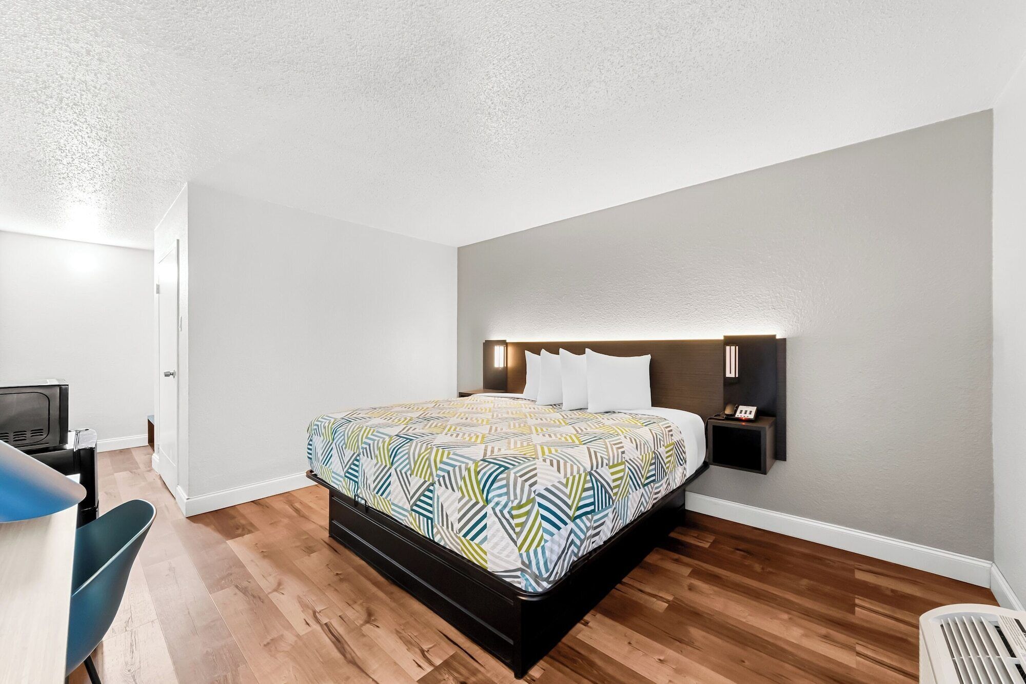 A hotel room with a bed, bedside table, and a desk with a chair.