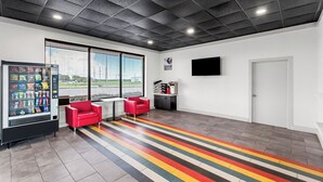 A modern interior with a vending machine, red chairs, a flat-screen TV, and a striped floor. - Motel 6 Port Lavaca, TX (Port Lavaca)