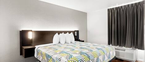 A modern hotel room with a large bed, a bedside table, a nightstand, a wall-mounted lamp, and a window with curtains.