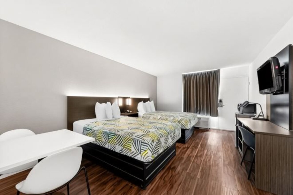 A hotel room with a bed, a desk, a chair, a TV, and a window with curtains.