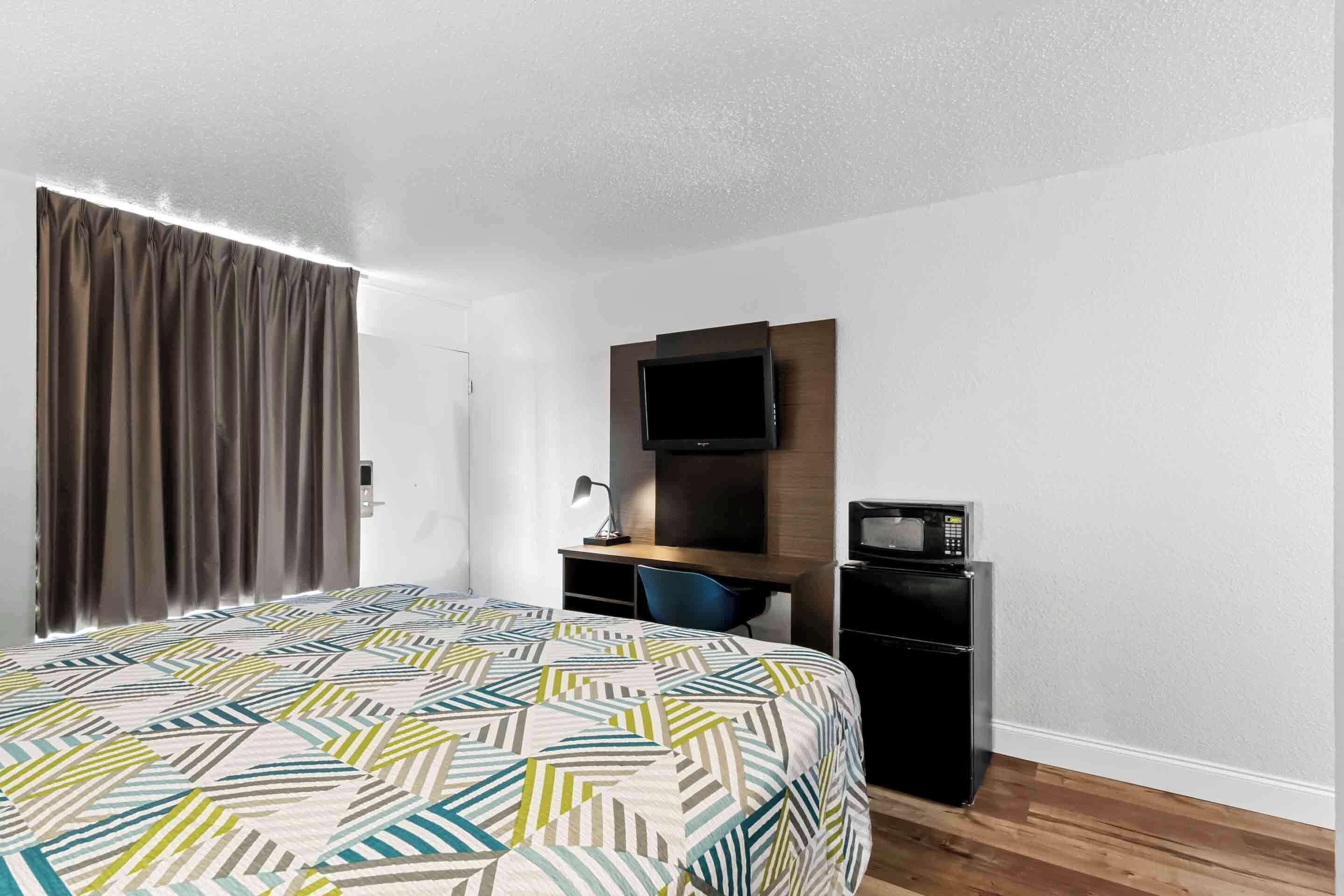 A hotel room with a bed, a desk with a computer, a TV, and a microwave.