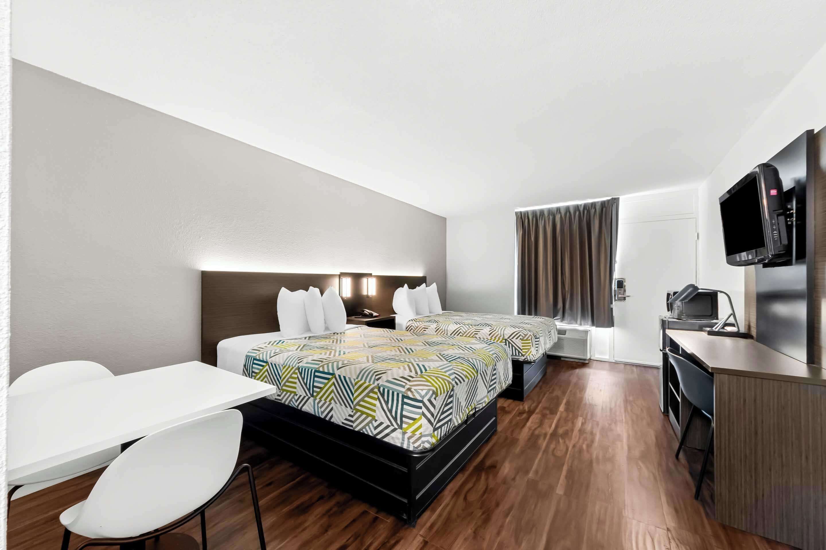 Habitación de hotel con dos camas, un escritorio, una silla, un televisor y una kitchenette.
