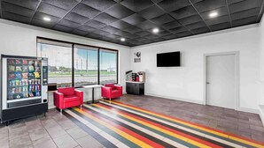 A modern interior with a vending machine, red chairs, a TV, and a striped floor. - Studio 6 Port Lavaca, TX (Port Lavaca)