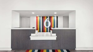 A reception area with a modern design, featuring a large number '6' on the wall, two reception desks, and a colorful striped wall behind them. - Studio 6 Port Lavaca, TX (Port Lavaca)
