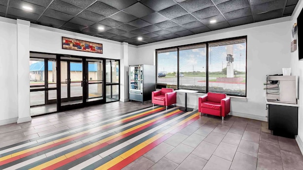 A modern lobby with a tiled floor, large windows, and red seating. - Studio 6 Port Lavaca, TX (Port Lavaca)