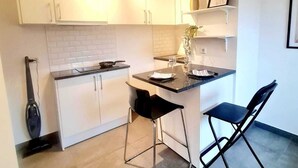 A compact kitchen with white cabinets, a black countertop, and a small island with two black bar stools. - New Studio in Center (Luxembourg City)