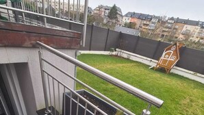 A residential outdoor area with a metal staircase leading to a balcony, a grassy yard, and a view of neighboring buildings. - New Studio in Center (Luxembourg City)