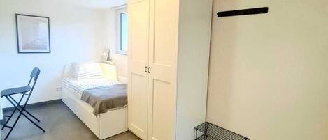 A small, well-lit room with a bed, a desk, and a wardrobe.
