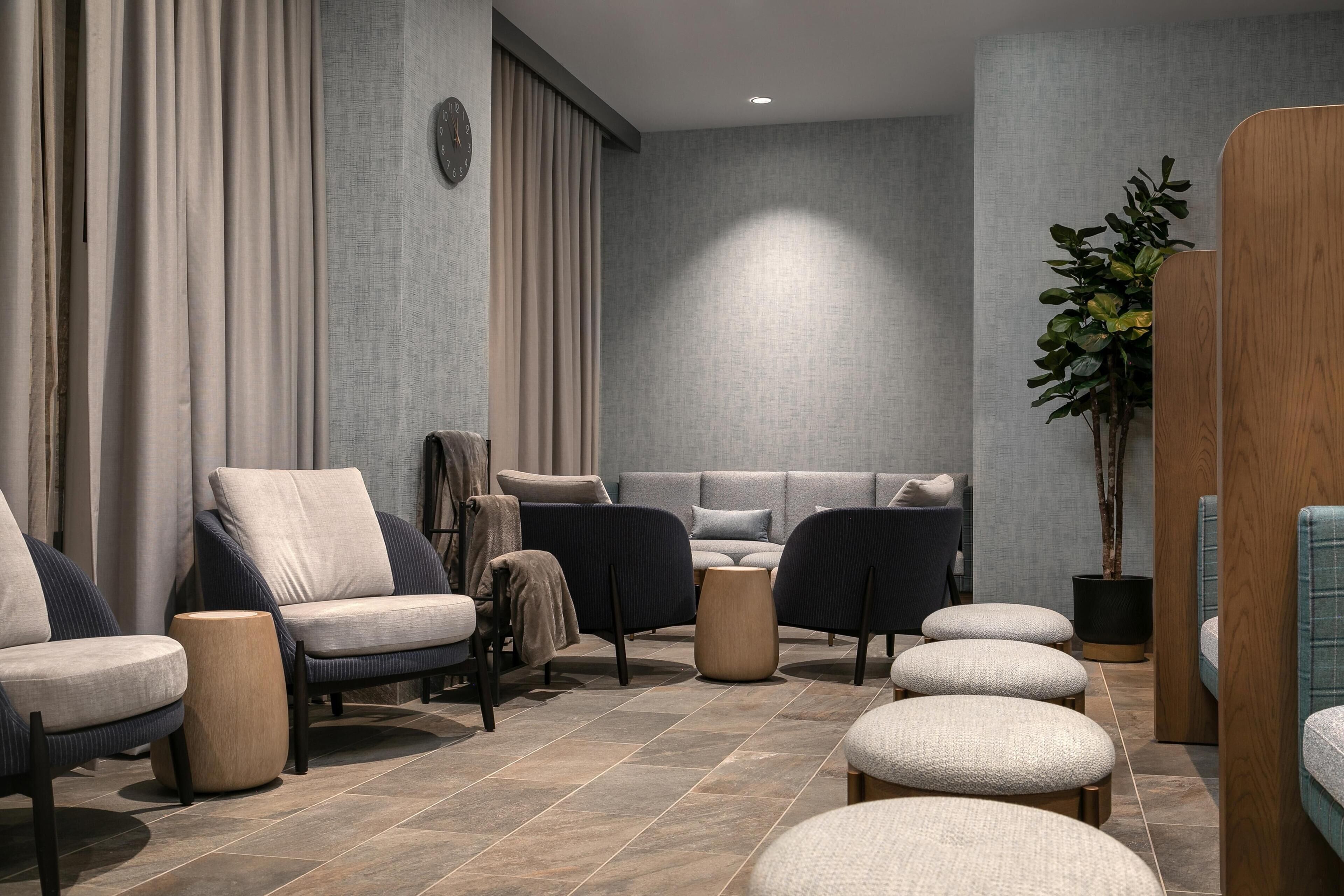 A modern lounge area with sofas, ottomans, and a potted plant.
