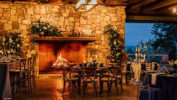 A stone-walled dining area with a fireplace, tables set for a meal, and chairs arranged around them.