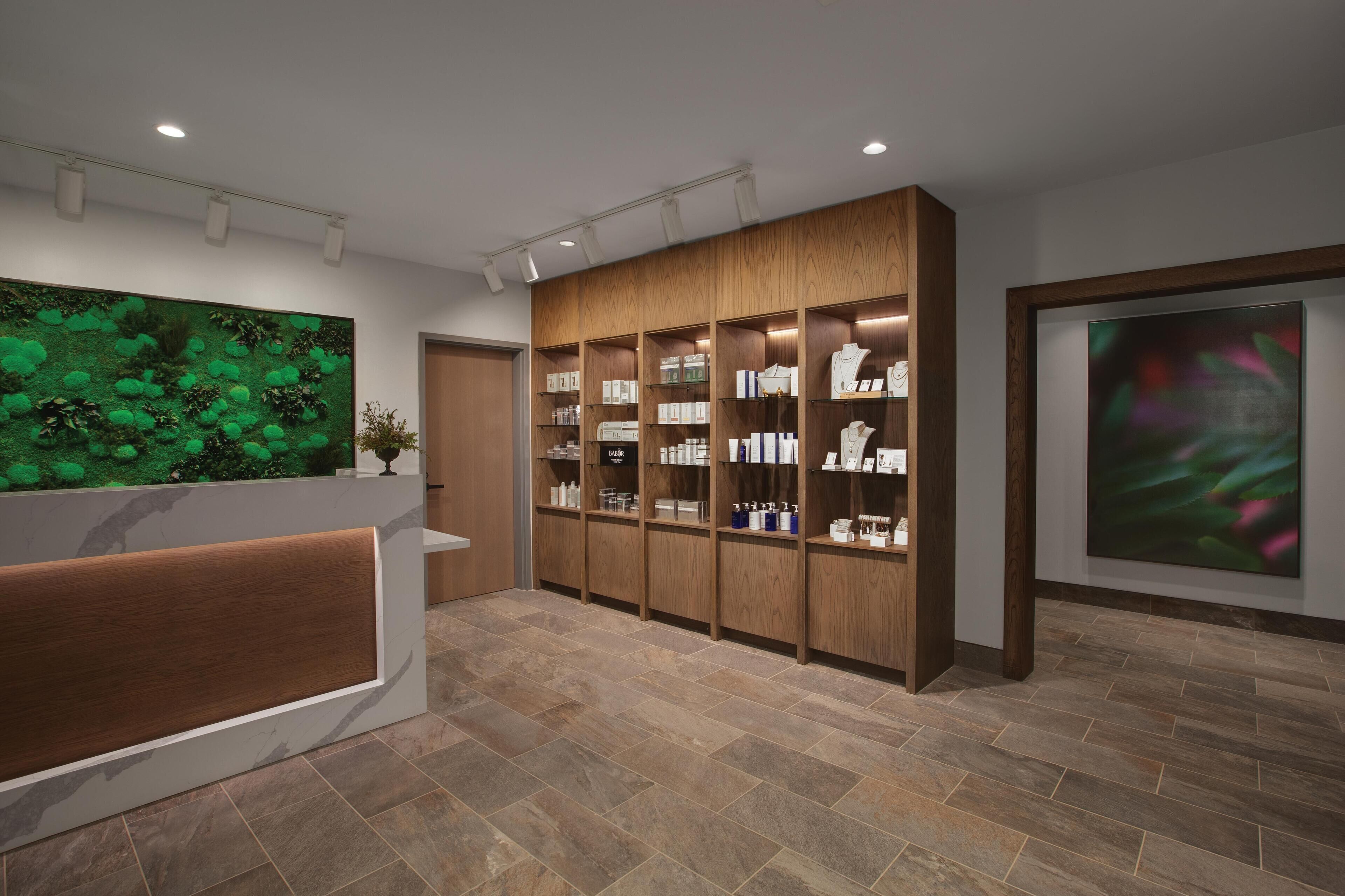 A reception area with a wooden reception desk, a green wall with plants, and a display of toiletries.