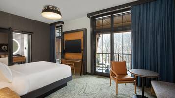 A hotel room with a large bed, a desk, a chair, a small table, and a large window with curtains.