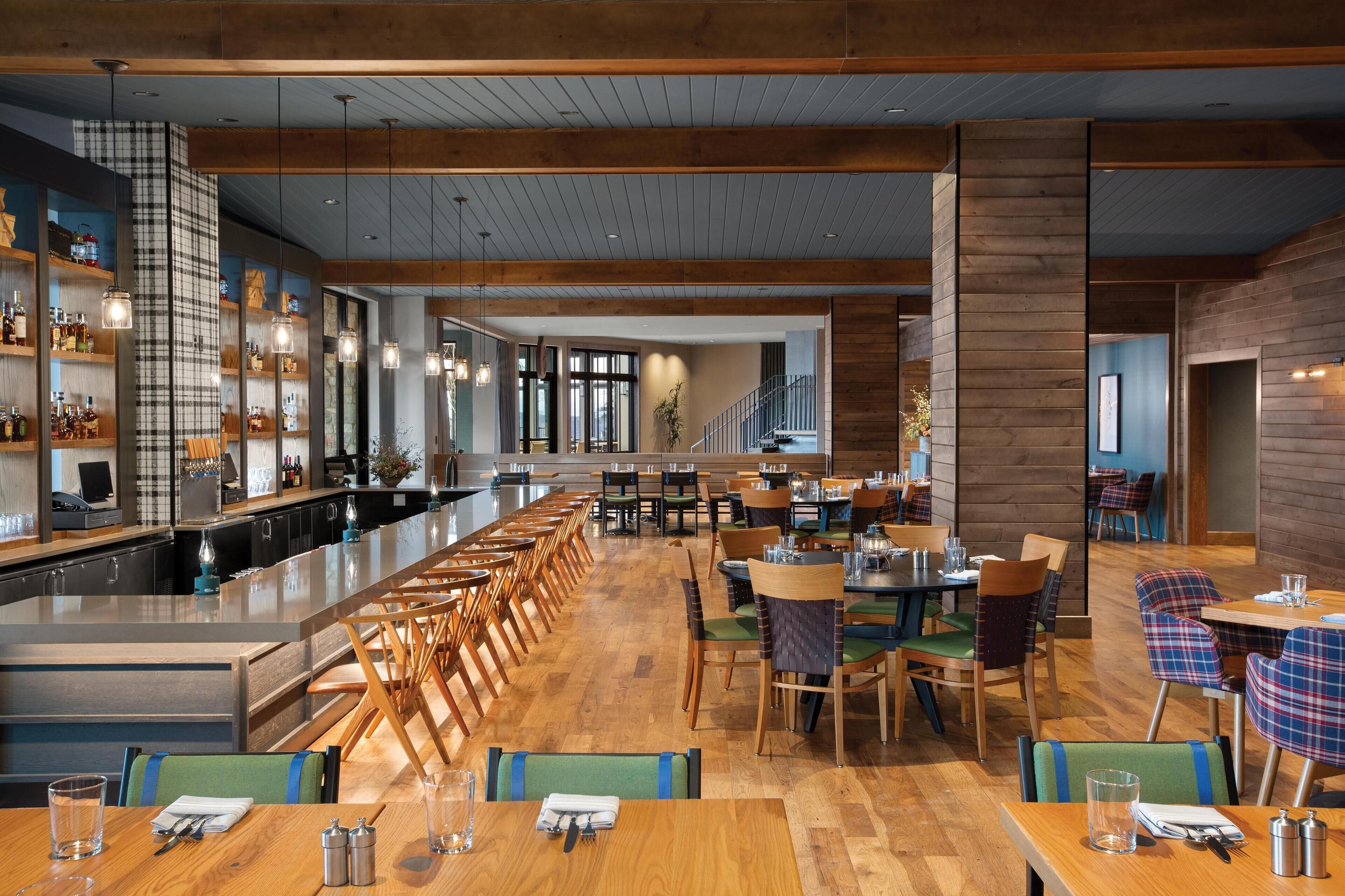 Un restaurant spacieux avec un long comptoir, de nombreuses tables et des chaises. Il y a également un bar avec des étagères remplies de bouteilles et une grande fenêtre qui laisse entrer la lumière naturelle.