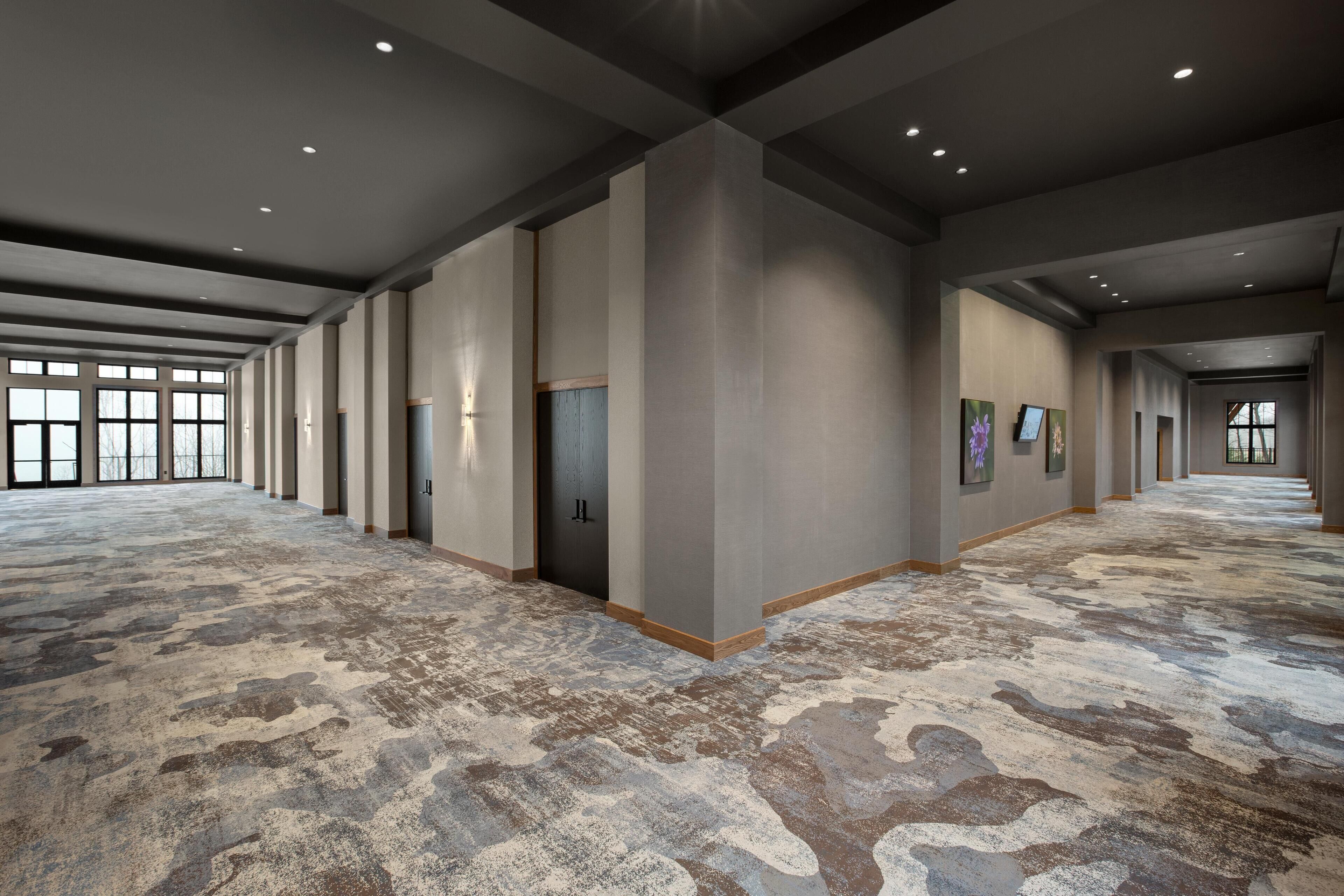 Un vaste couloir d’hôtel, agrémenté d’un tapis à motifs, d’un éclairage encastré et d’œuvres d’art encadrées accrochées aux murs.