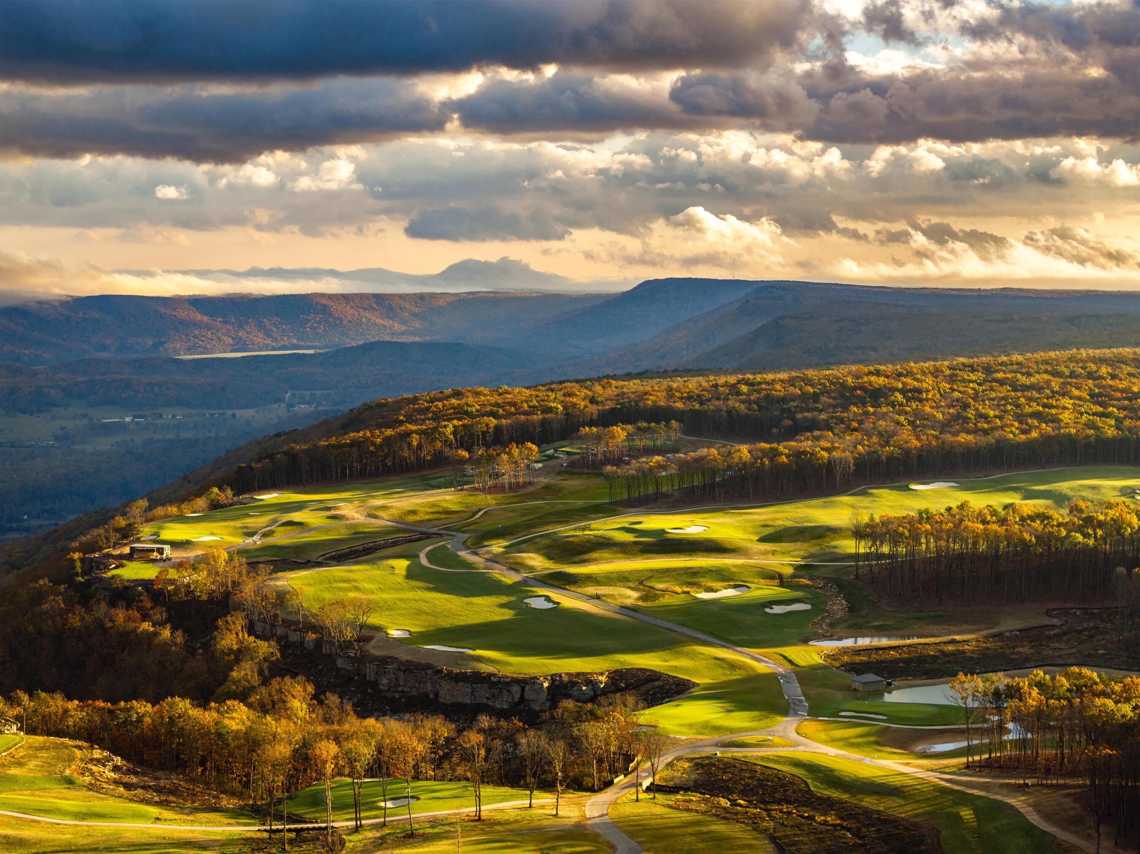 A golf course with a scenic view of mountains and a lake in the distance.