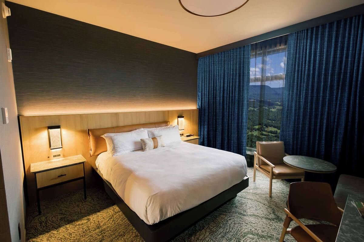 A hotel room with a large bed, bedside tables with lamps, a round table, and a view of the outdoors.