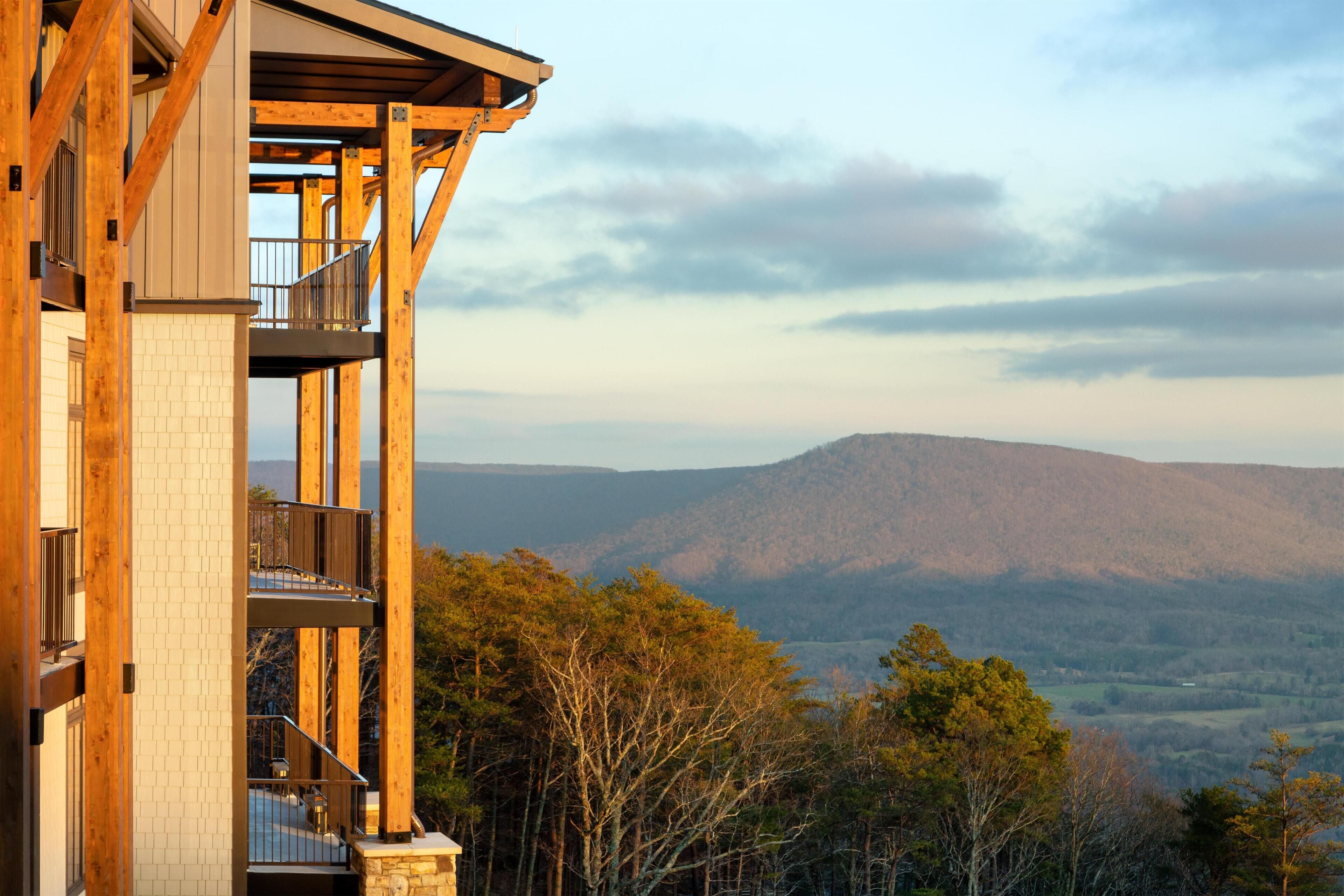 Un immeuble à plusieurs étages doté d’un balcon, entouré d’arbres et situé dans un paysage montagneux.