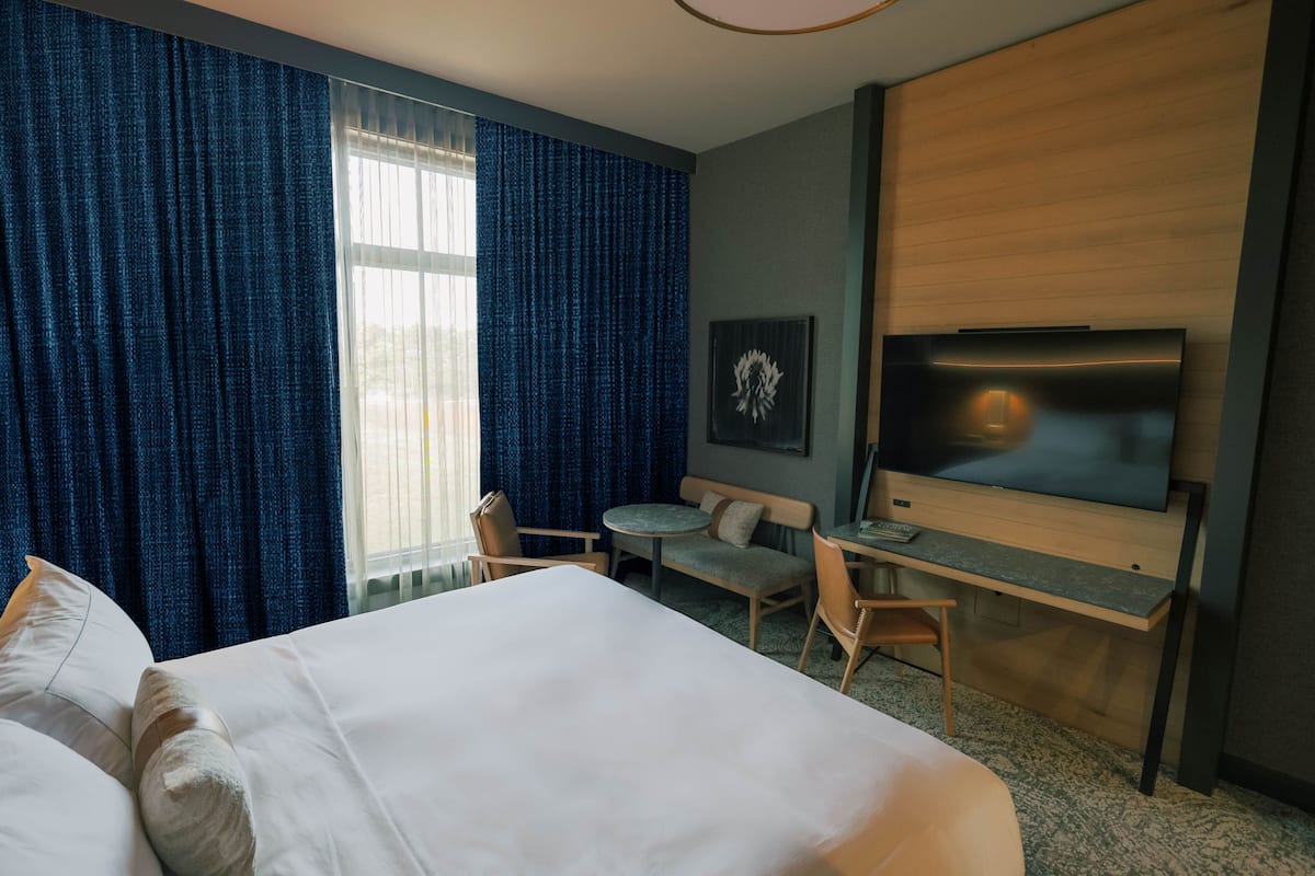 A hotel room with a large bed, a desk, a chair, a television, and a window with curtains.