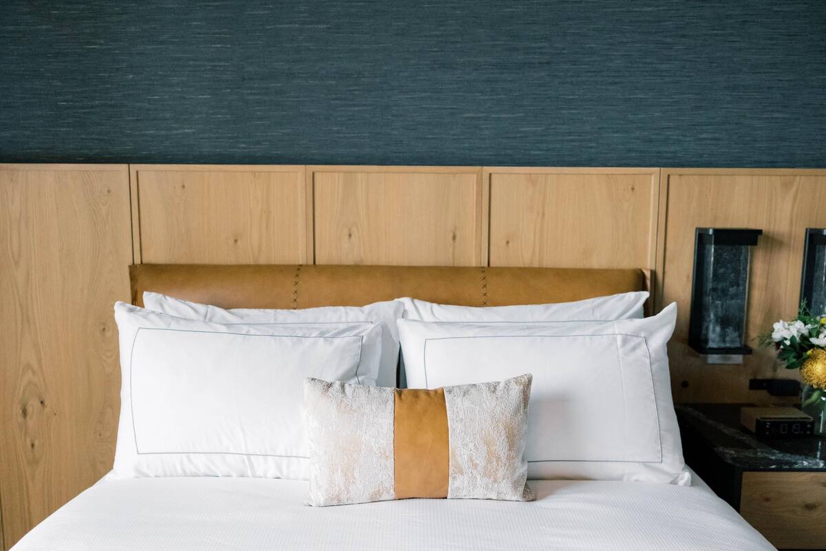 A neatly made bed with white linens and two pillows, one with a brown accent.