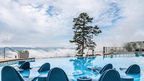 Piscina con sillones de descanso, un árbol y vistas de nubes.
