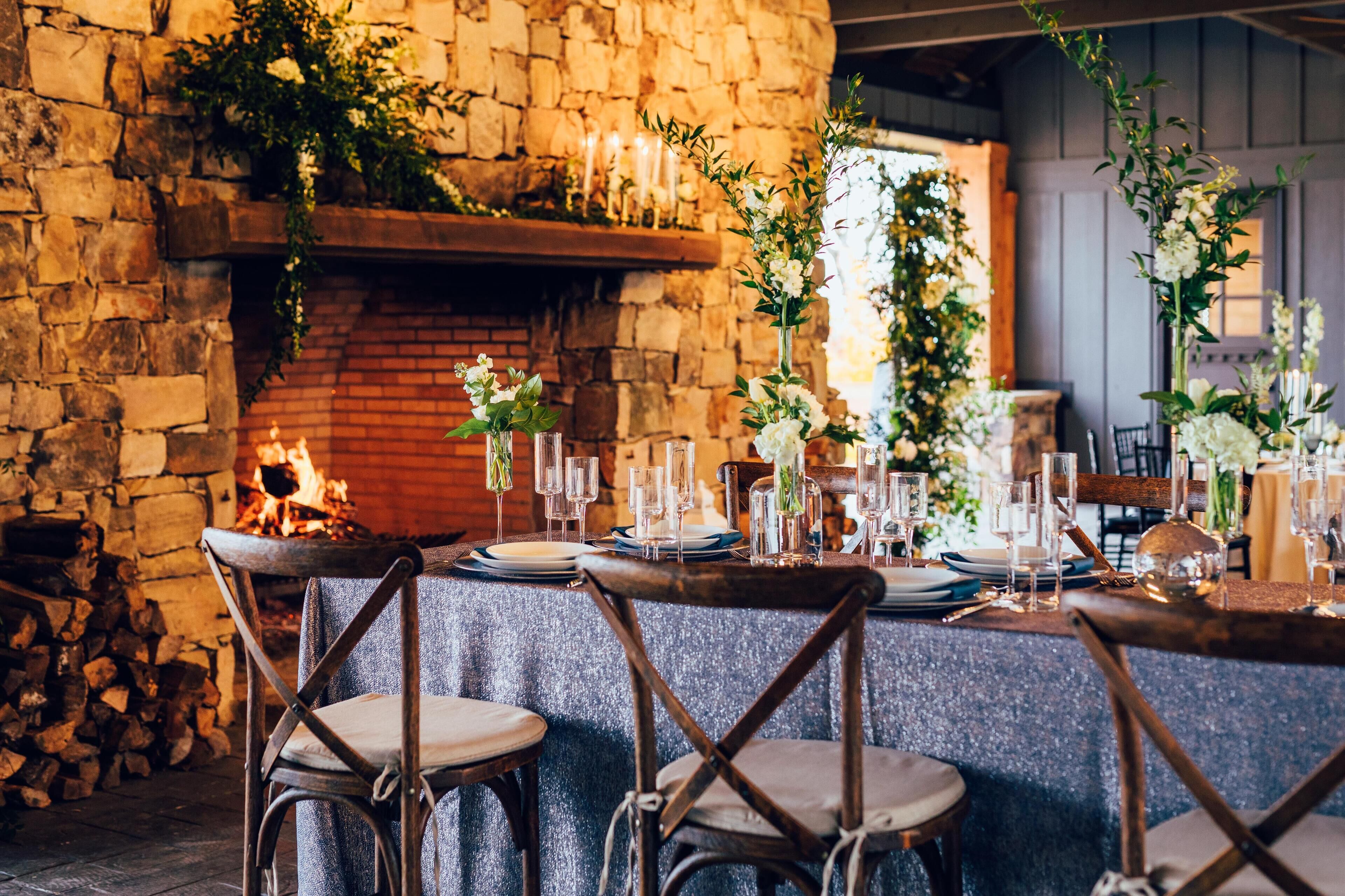 A rustic dining area with a stone wall, a fireplace, and a long table set for a meal.