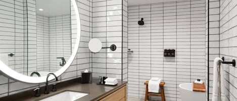A modern bathroom with a large mirror, two sinks, a wooden vanity, a toilet, and a bathtub.