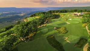 Un campo de golf con un club de campo, rodeado de exuberante vegetación y colinas.
