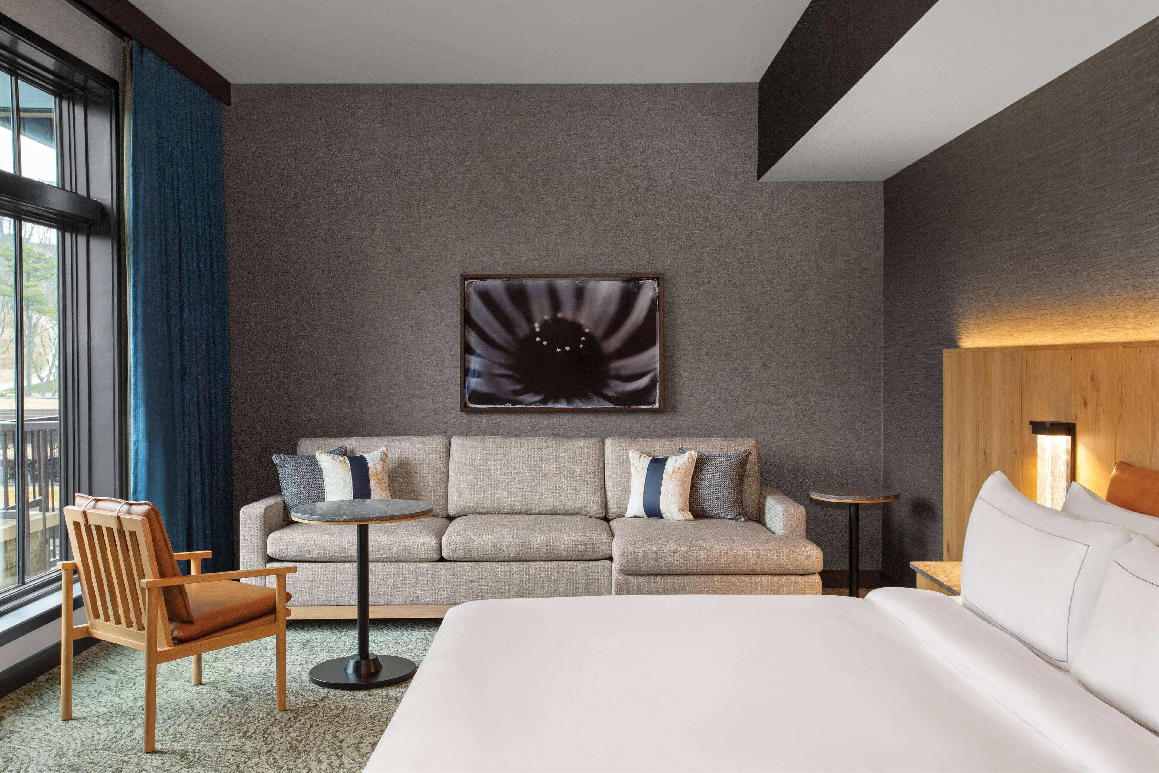 Et moderne hotelværelse med en stor seng, en sofa, en stol, et rundt bord og et kunstværk på væggen.