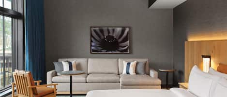 Et moderne hotelværelse med en stor seng, en sofa, en stol, et rundt bord og et kunstværk på væggen.