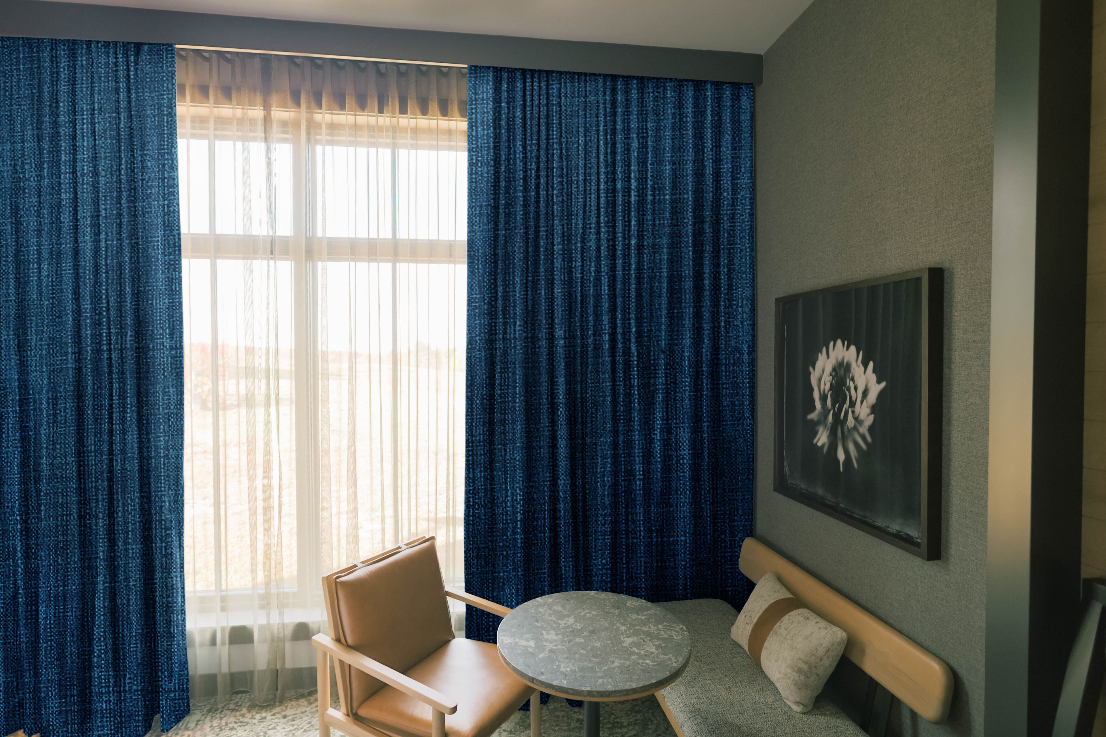 A room with a large window, a chair, a small round table, a sofa, and a wall-mounted artwork.