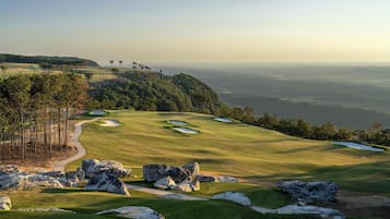 Un campo de golf con un sendero serpenteante, búnkeres de arena y vistas a colinas distantes.