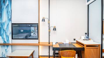 Una habitación de hotel moderna con un escritorio de madera, un banco, una silla amarilla, un televisor de pantalla plana montado en la pared y un ventanal grande.