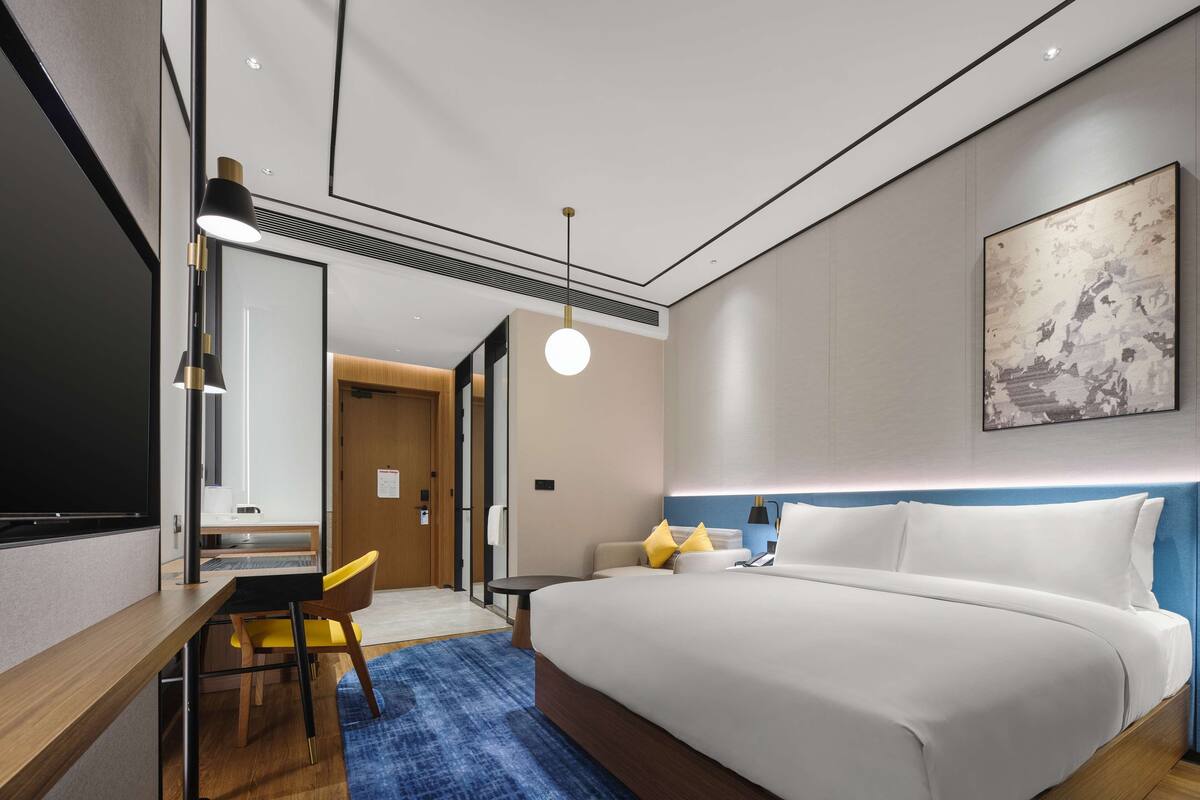 Habitación de hotel moderna con una cama grande, un escritorio con silla, un espejo y un tapete azul.