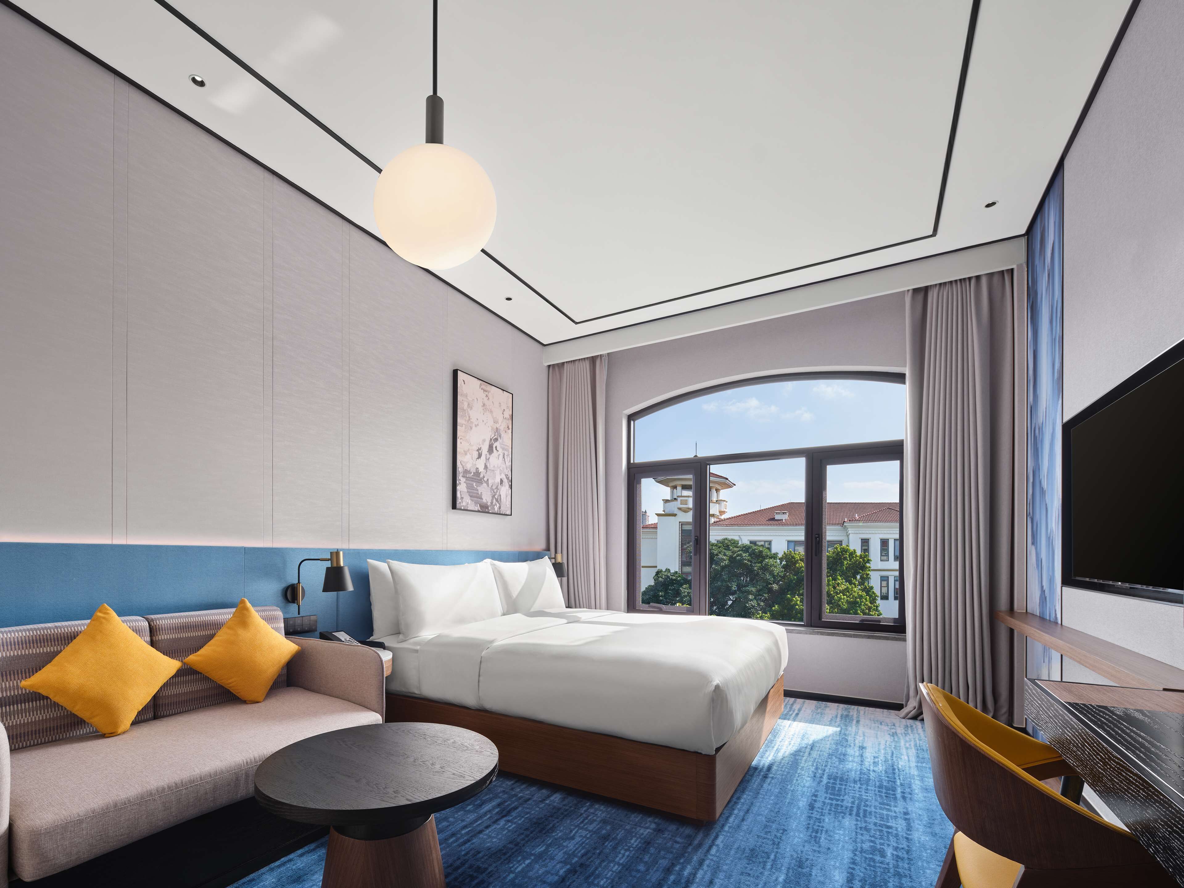 A modern hotel room with a bed, sofa, and a round table.