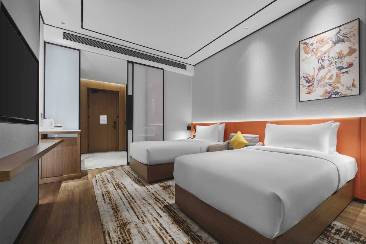 Una habitación de hotel moderna con dos camas, un escritorio y un cuadro abstracto grande en la pared.