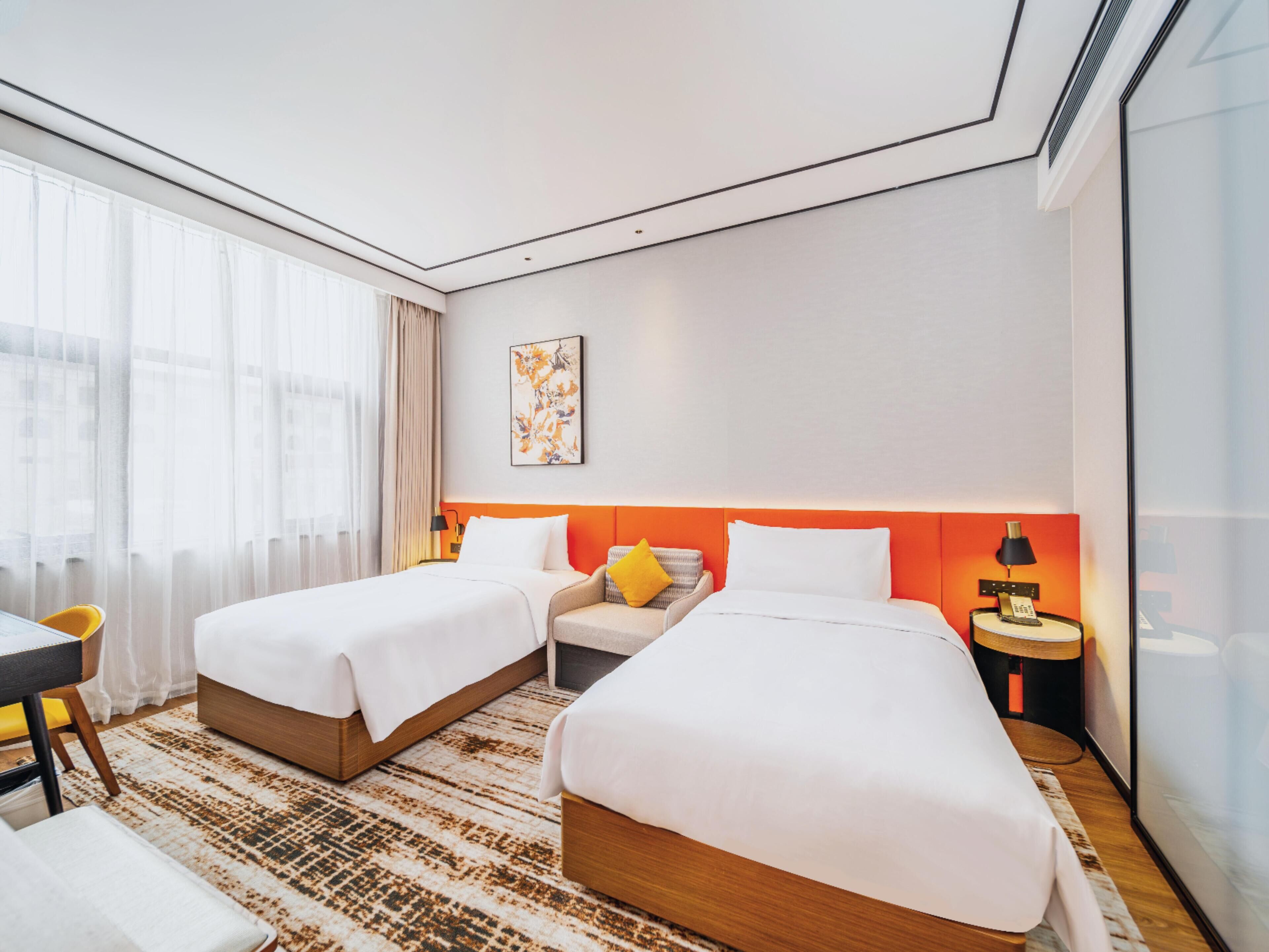 A hotel room with two beds, a desk, a chair, a nightstand, and a large window with curtains.