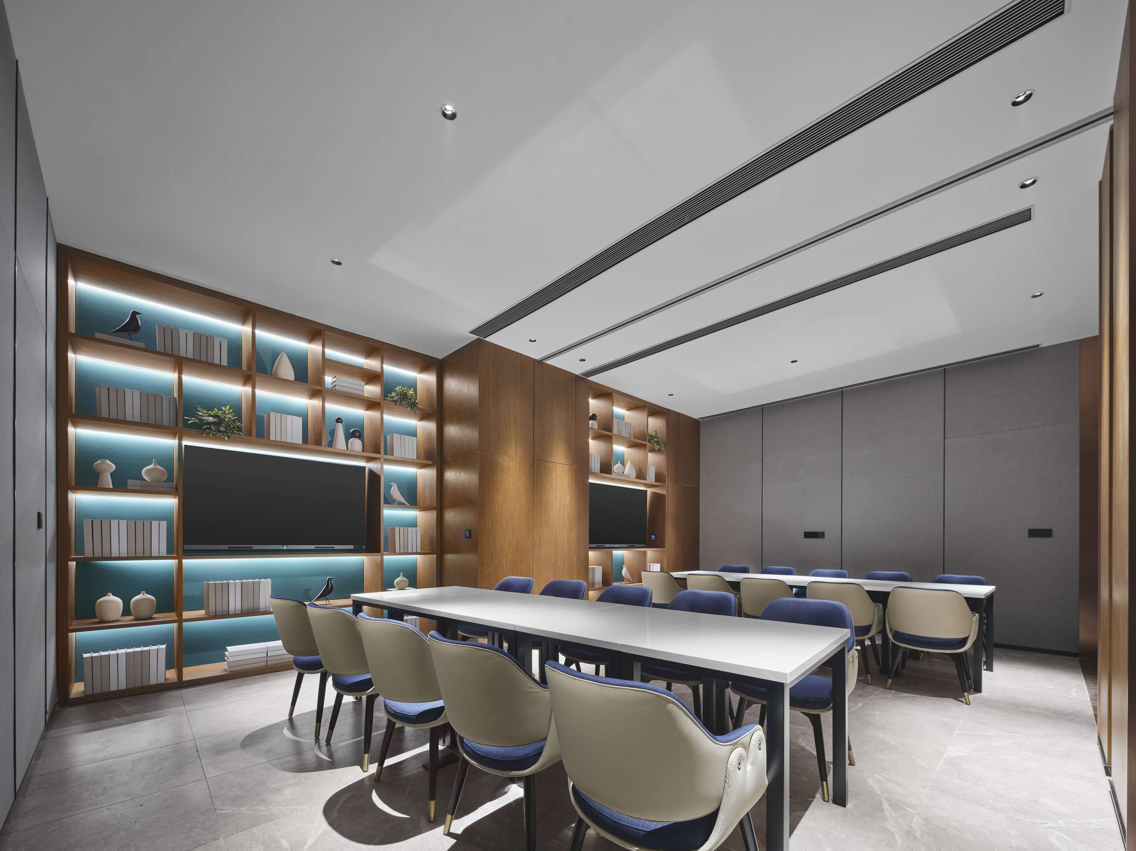 Une salle de conférence moderne, dotée d’une longue table, de chaises et d’étagères intégrées où sont exposés des objets décoratifs.