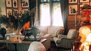 A cozy living room with patterned furniture, a decorative lamp, and framed artwork on the walls.