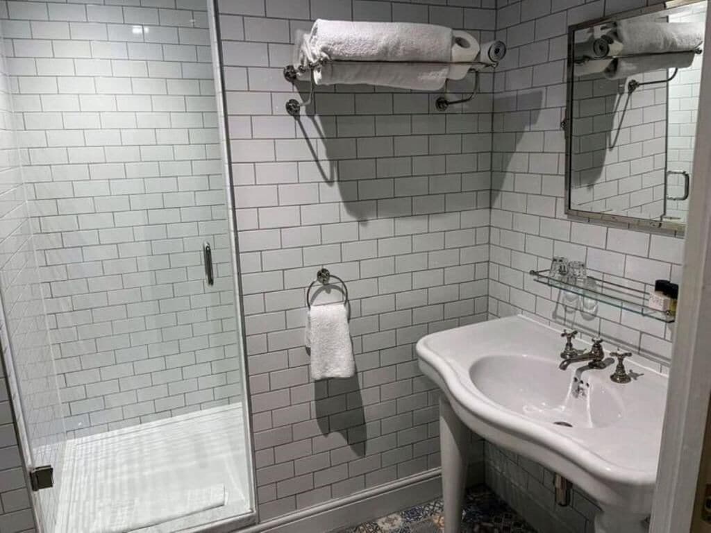 A bathroom with a glass shower enclosure, a sink with a mirror, and two towel racks.