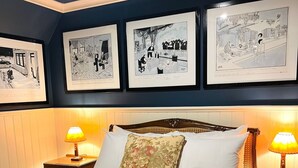 A neatly made bed with floral pillows, two bedside lamps, and three framed black-and-white illustrations on the wall.