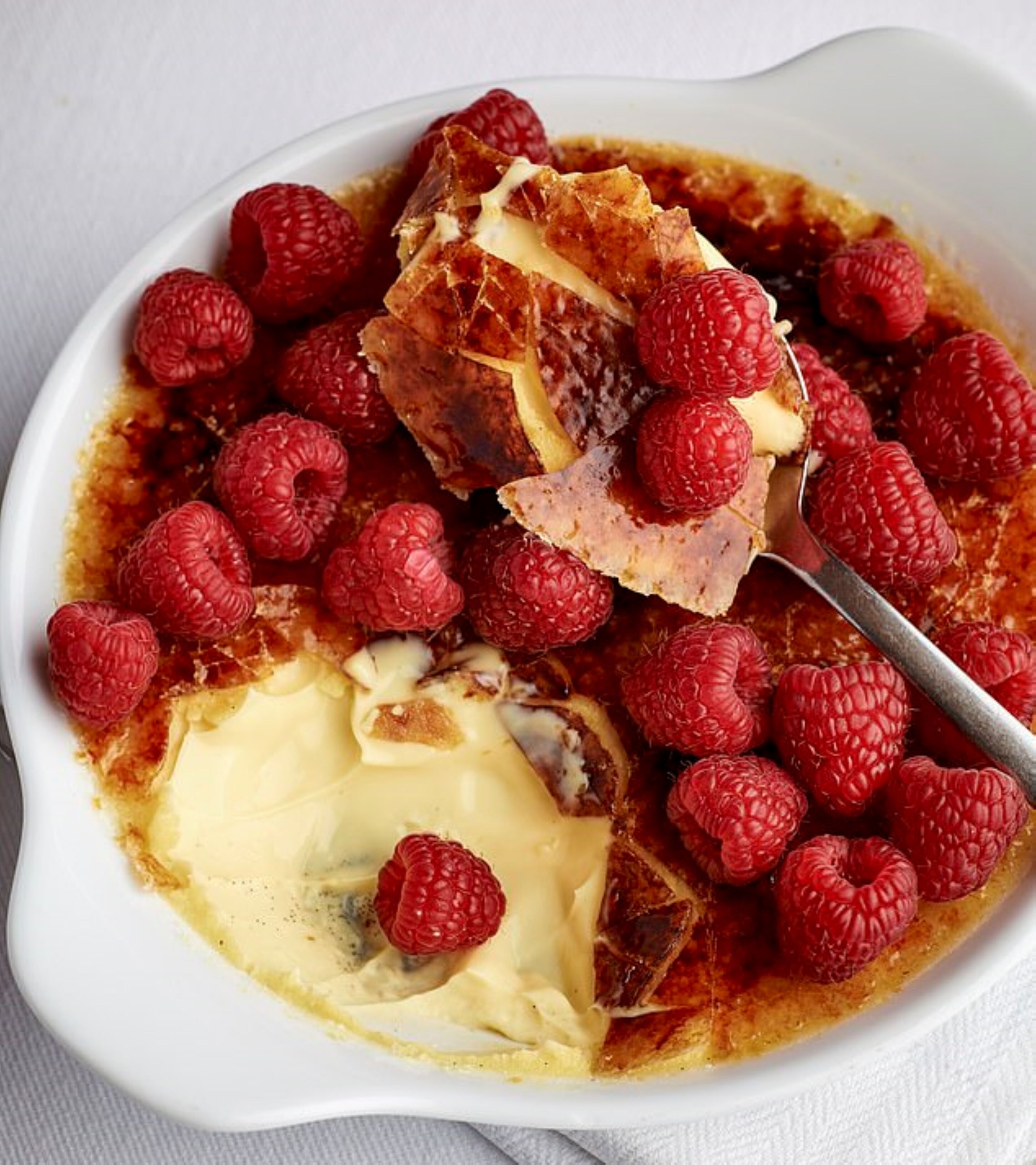 Un dessert aux framboises, accompagné d’une boule de glace, servi dans un bol blanc.