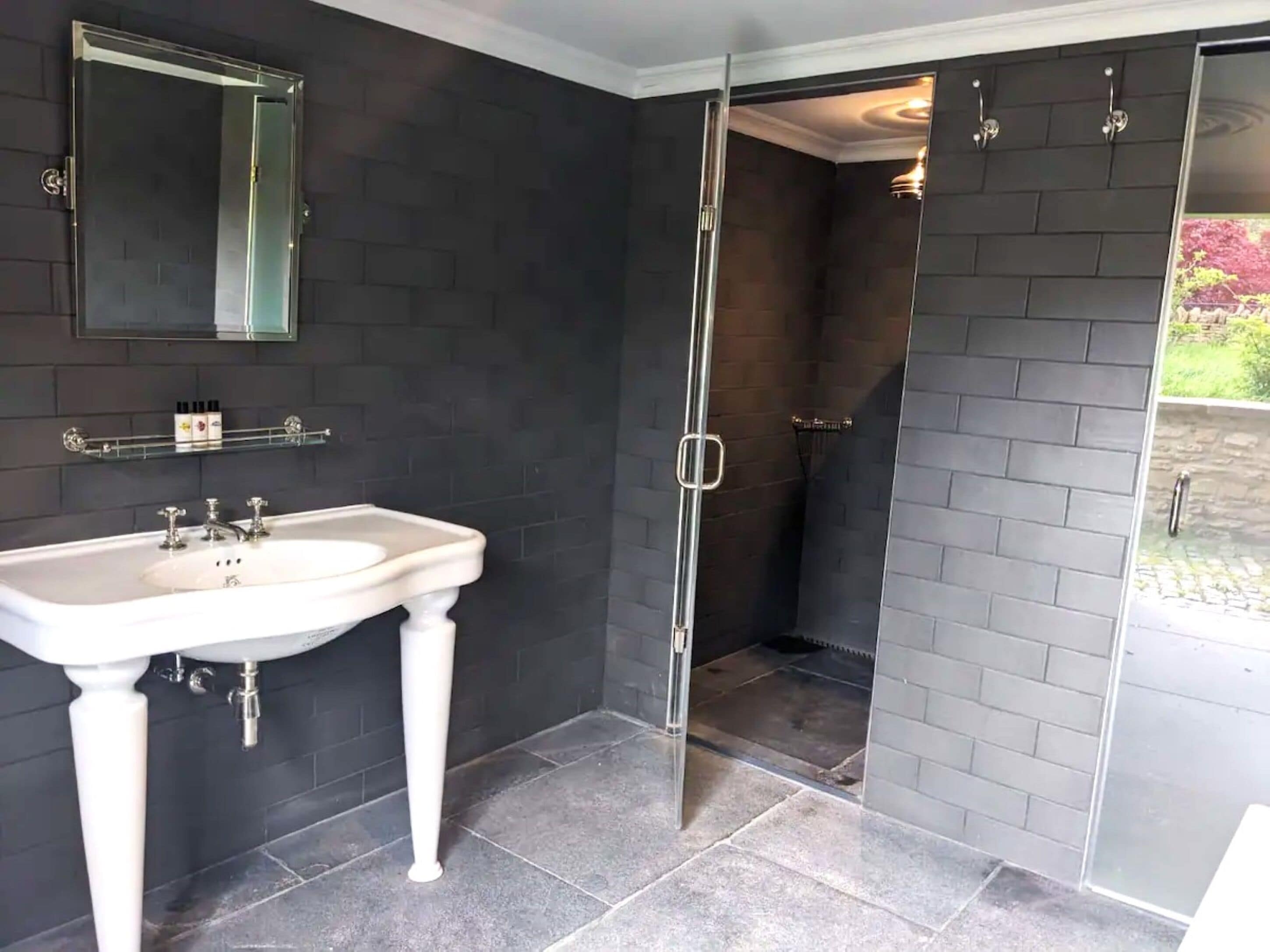 A bathroom with a white pedestal sink, a mirror, and a glass-enclosed shower.