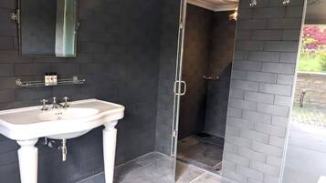 Une salle de bain avec un lavabo sur pied blanc, un miroir et une douche à parois de verre.