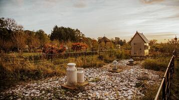 Un espacio rústico al aire libre con un sendero de grava, estructuras de piedra y un pequeño edificio de madera.