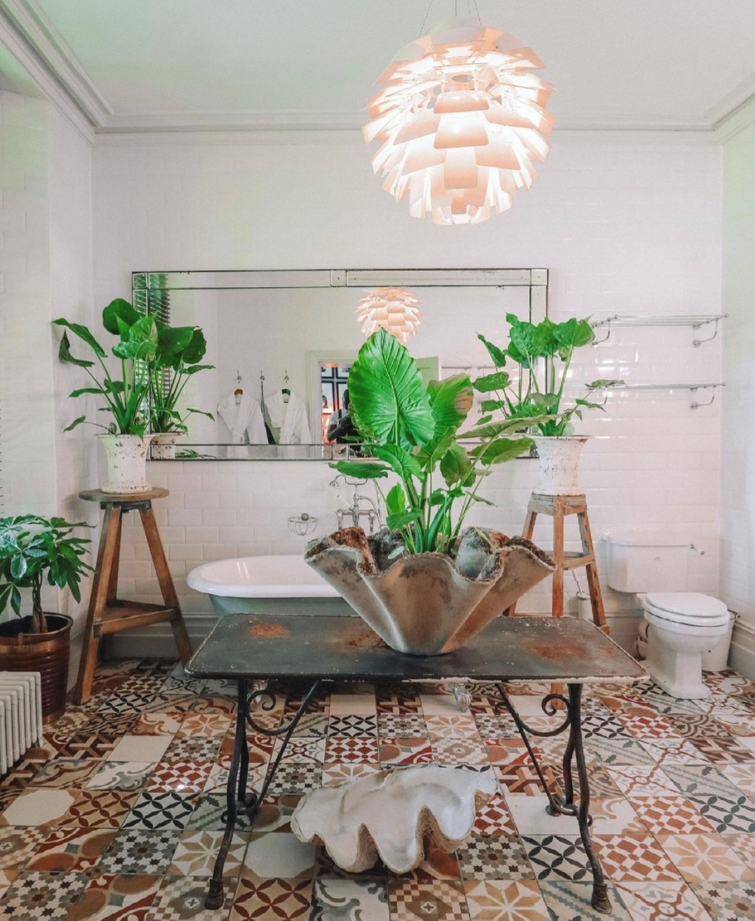 Casa de banho com uma pia branca, um espelho grande e plantas em vasos.