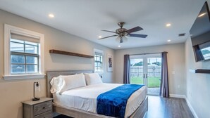 A bedroom with a bed, a nightstand, a ceiling fan, and a large window with curtains.